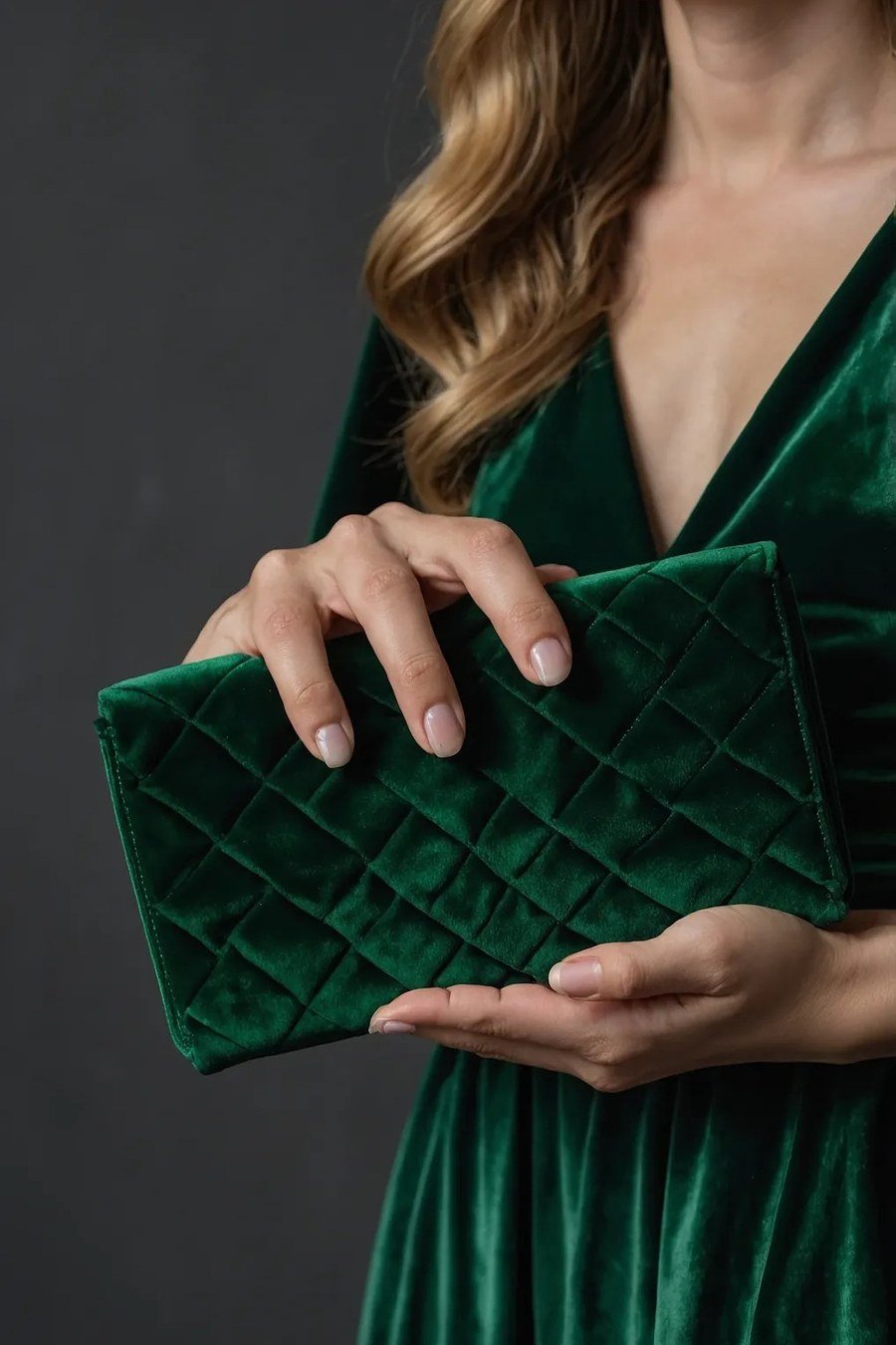 Quilted emerald green velvet clutch held in hand