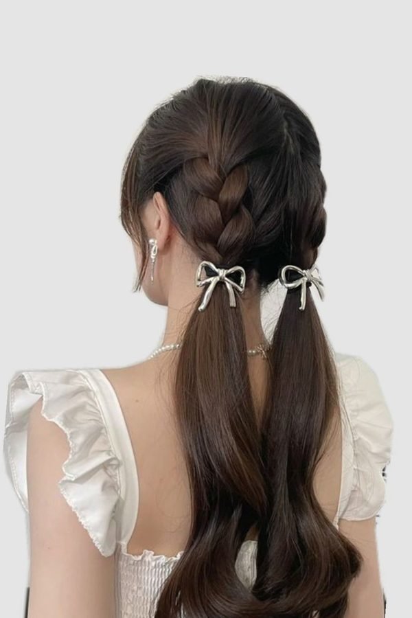 Twin low ponytails with mini white bows on dark wavy hair