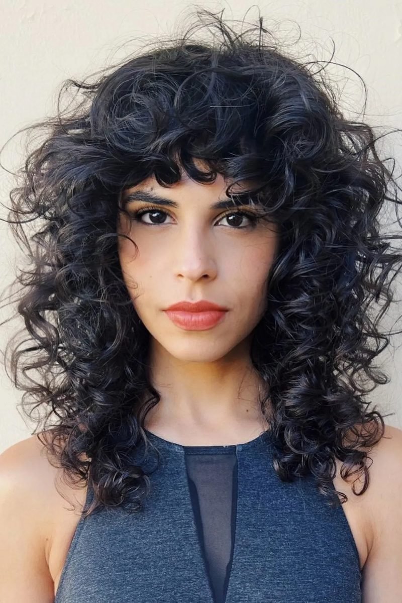 Voluminous black curly wolf cut with full bangs, front view