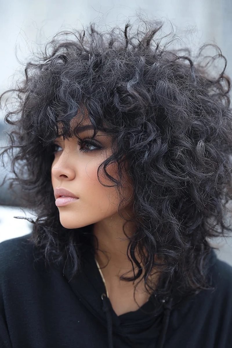 Medium-length black fluffy curly wolf cut, side view