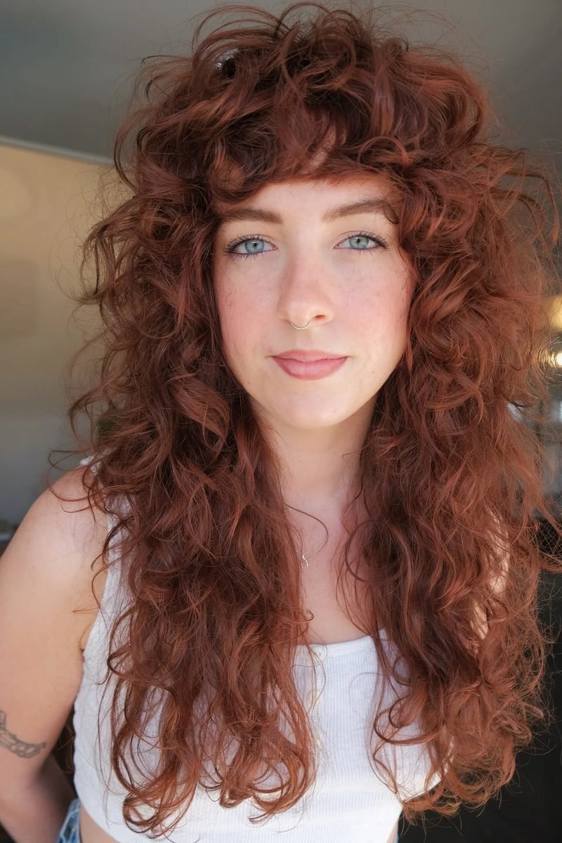 Long copper-red curly wolf cut with soft bangs, front view