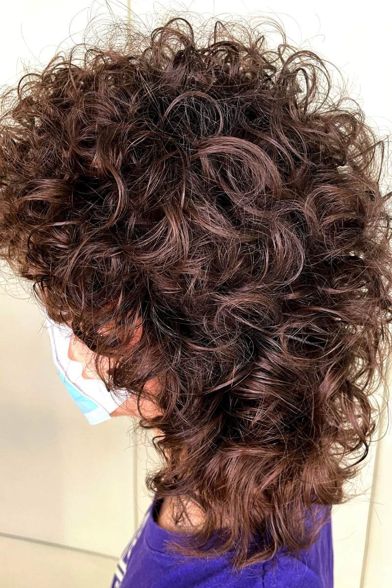 Dark curly wolf cut from back and side in a salon