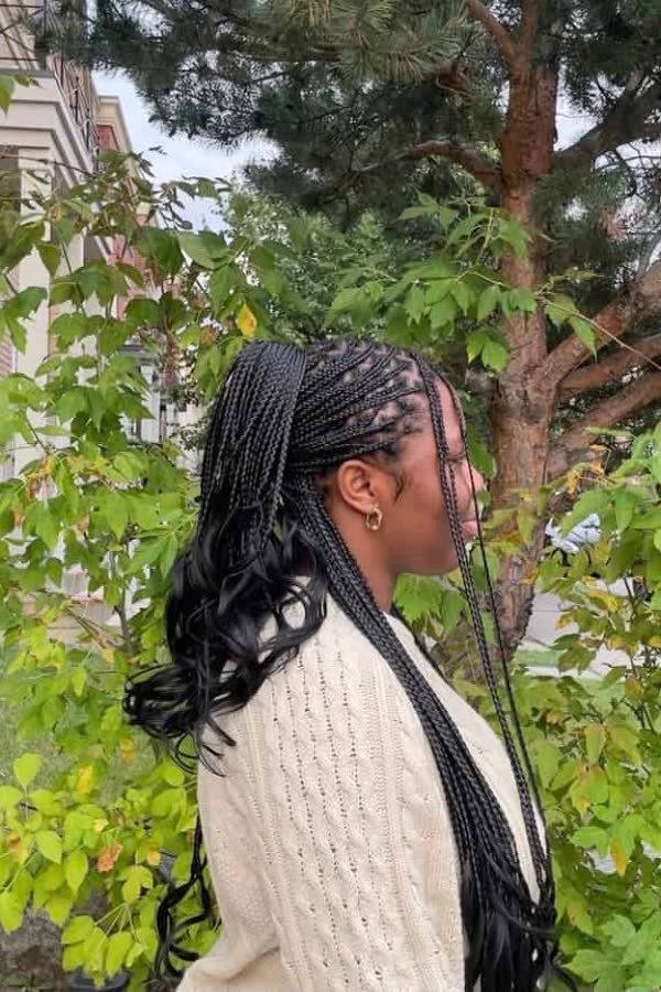 Side profile of long black french curl braids swept to one side outdoors