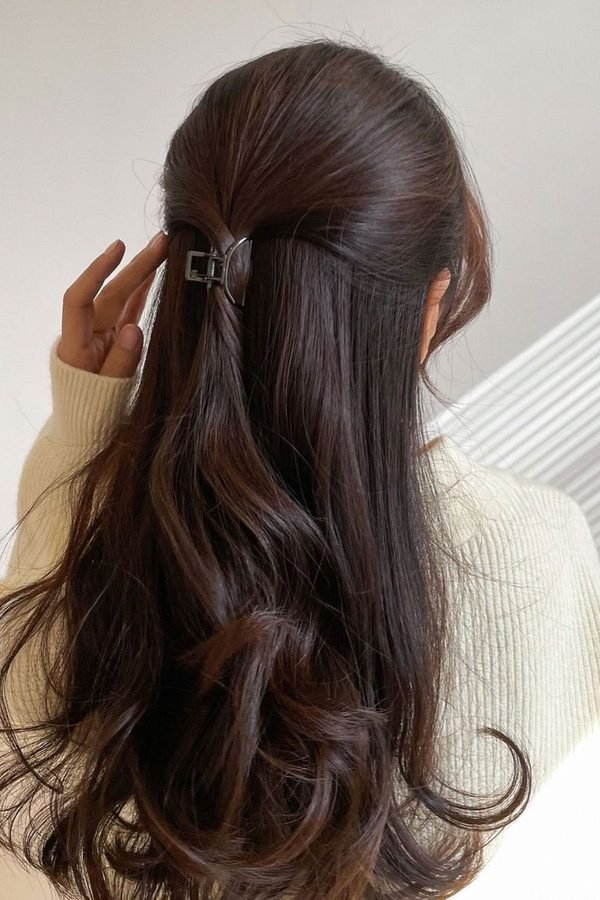 Half-up hairstyle secured with a small claw clip on dark wavy hair, back view