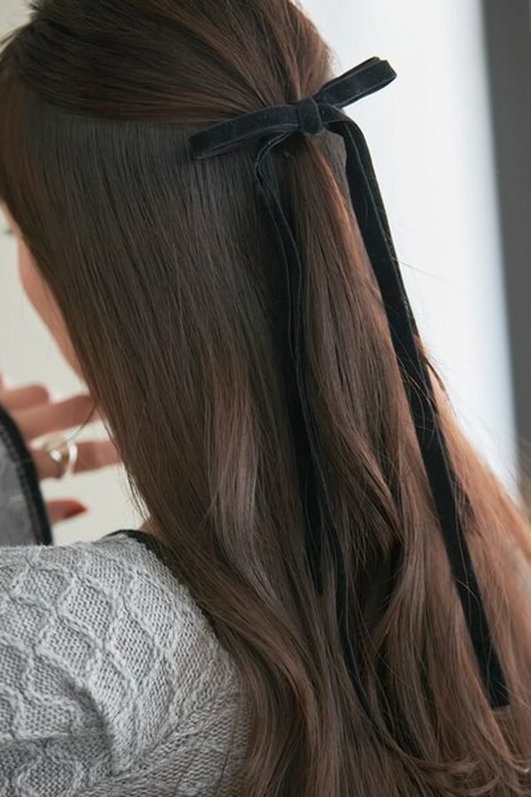 Half-up hairstyle tied with a black velvet bow on long brown waves, back view
