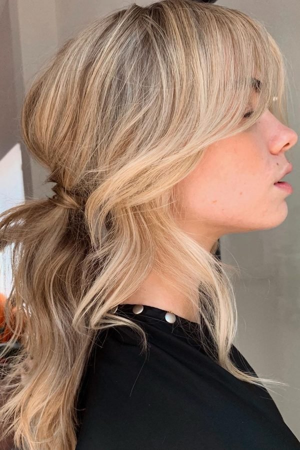 Half-up low ponytail with curtain bangs on blonde hair, side profile