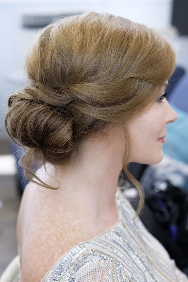 Rolled low bun with soft crown volume, side profile on a mature woman