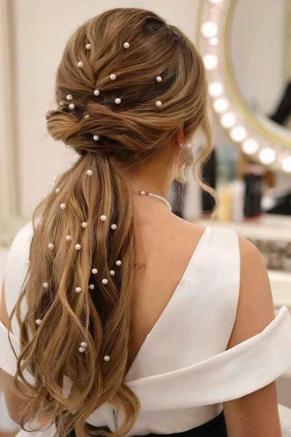 Low wavy ponytail decorated with pearl pins, wedding guest style