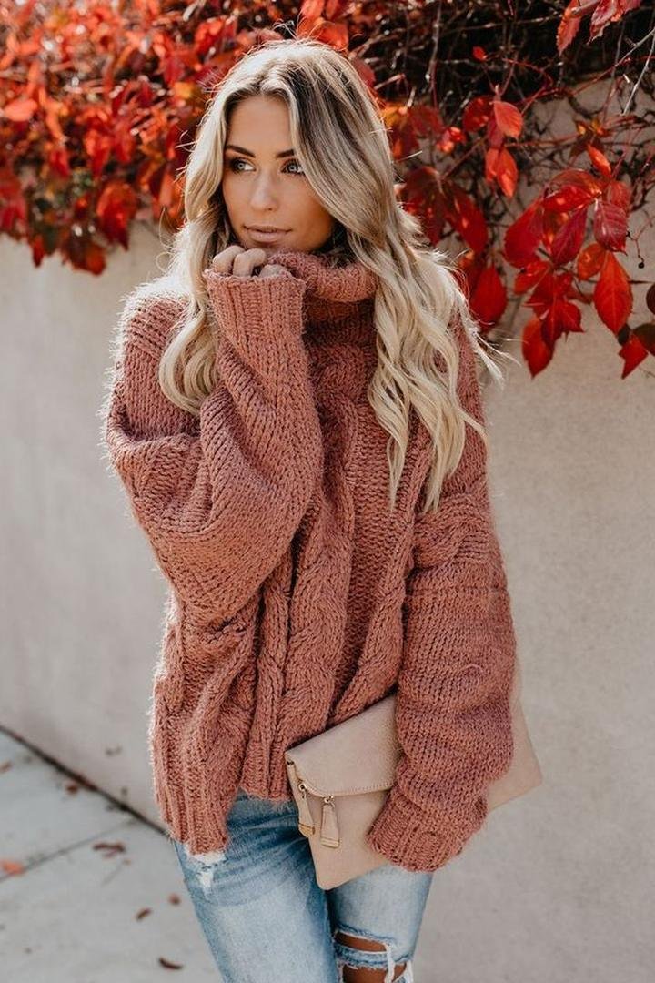 Woman wearing a rust chunky cable-knit turtleneck sweater with jeans among autumn leaves – thanksgiving outfits women