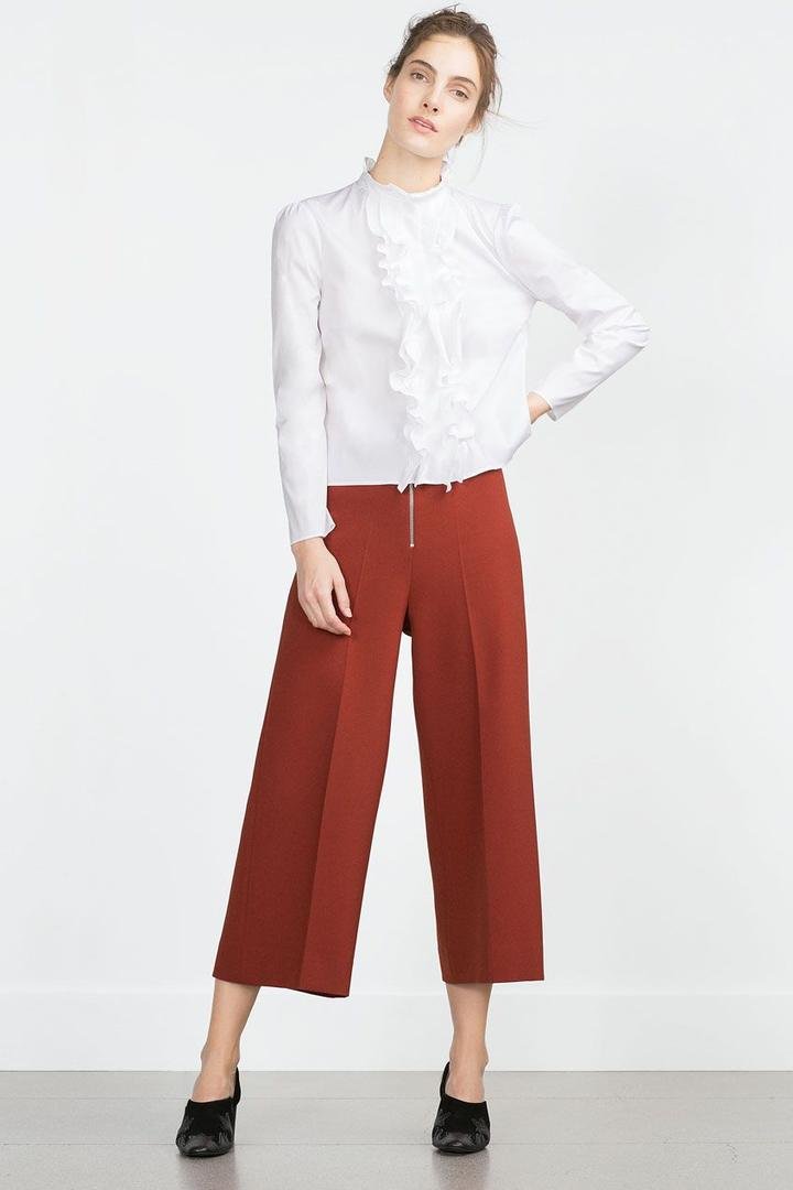 White ruffled blouse with rust wide-leg cropped trousers and black flats