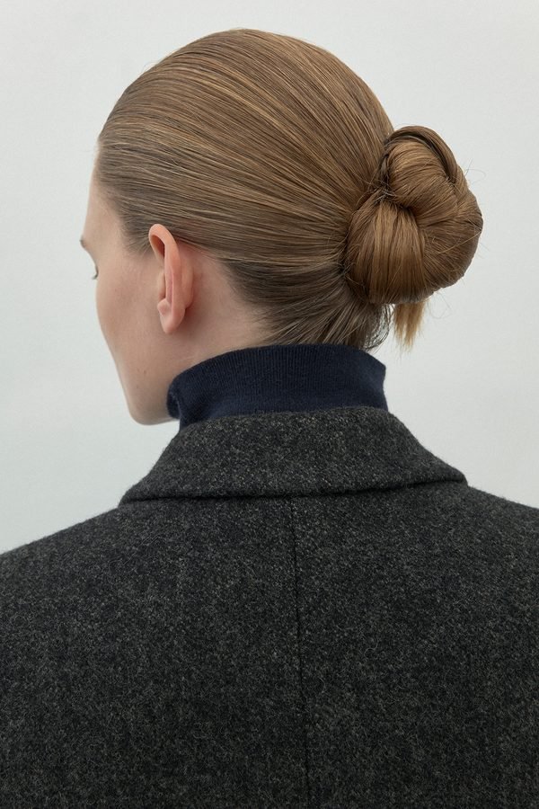 Sleek low bun tucked neatly above a winter coat collar, back view
