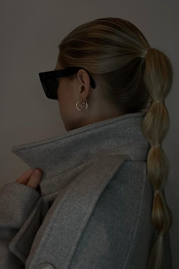 Low ponytail tucked into a raised grey coat collar, back view